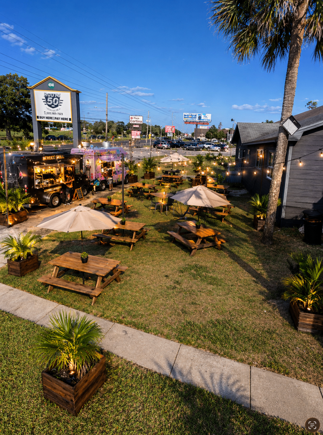 Wooden picnic tables on the grass with planters and string lights at The Yard 4540